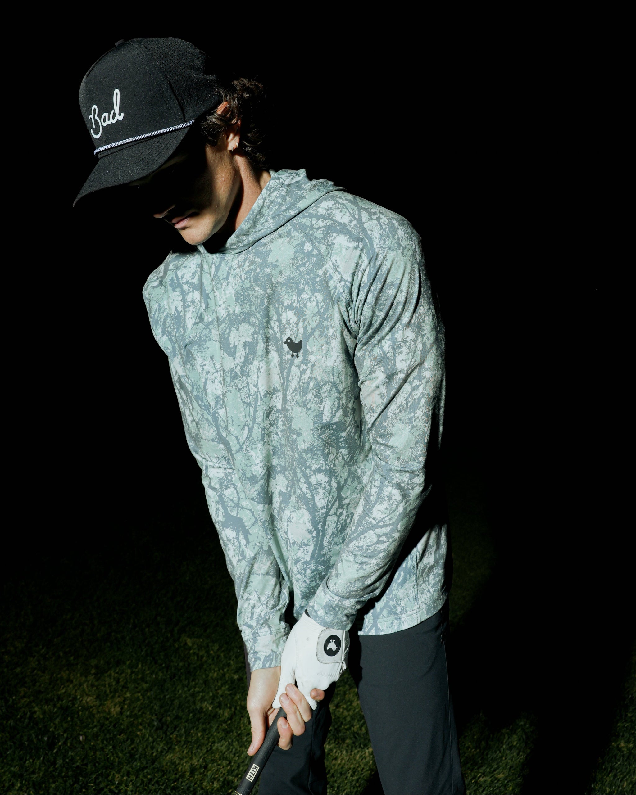 Person wearing a light green patterned jacket and dark cap on a black background