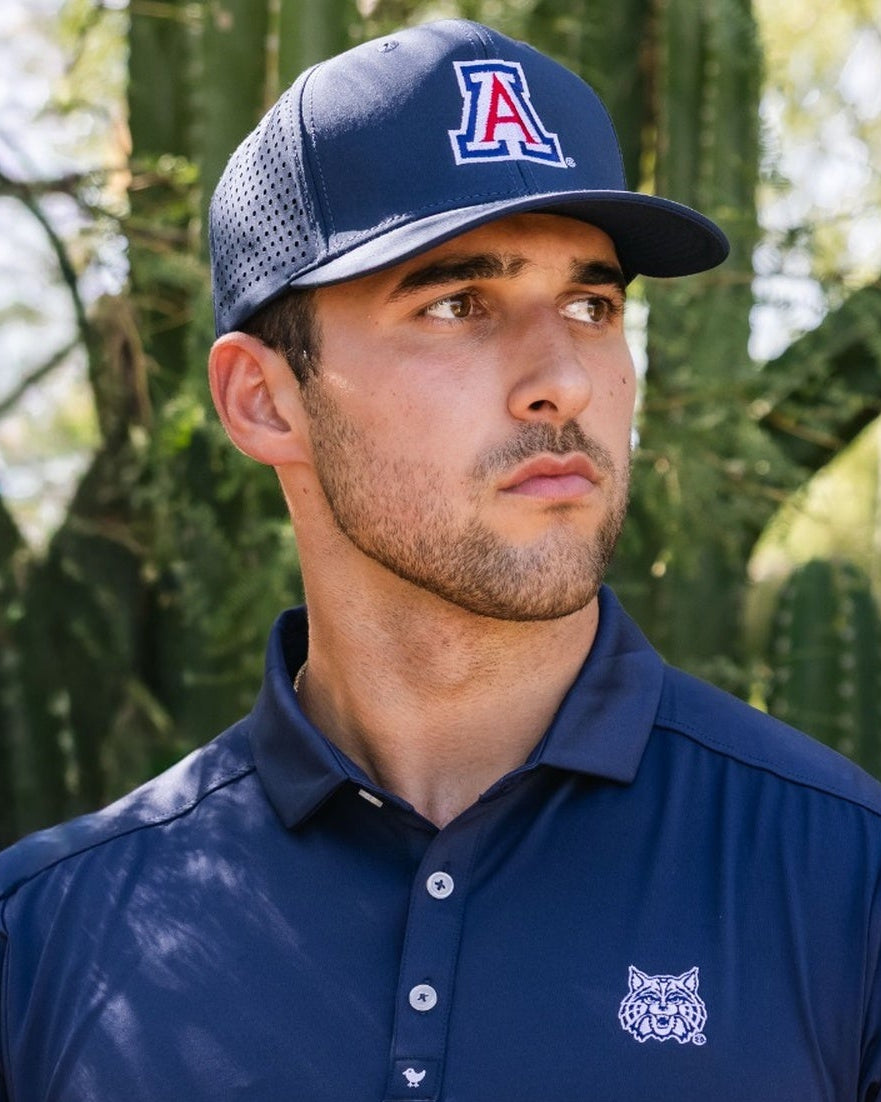 Man wearing a navy blue polo shirt and cap with cacti in the background